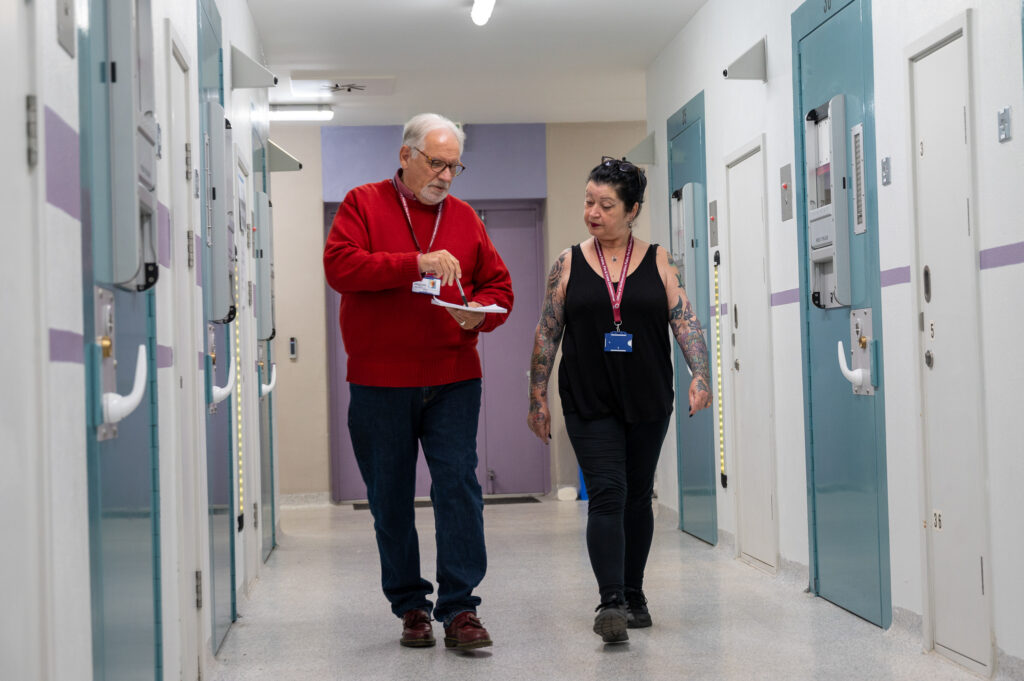 Independent Custody Volunteers Steve Edwards (left in red jumper) and Rachel Nash (right in black top) are shown walking down a wing in the Criminal Justice Centre in Northampton