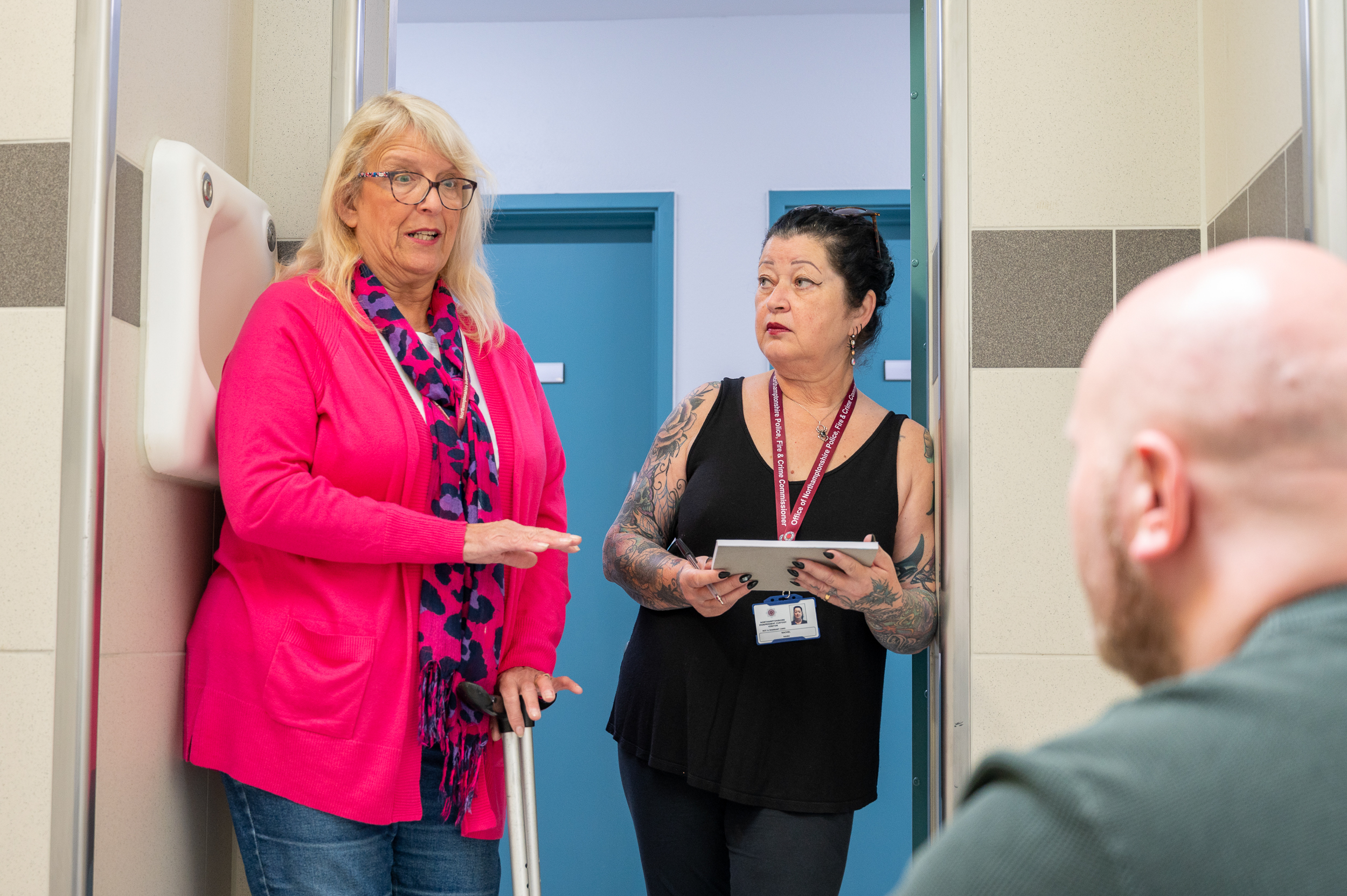 Independent Custody Volunteers Catherine Broughton (left in pink jacket) and Rachel Nash (right in black top with clipboard) speak to a person in a green jumper who is in custody at the Criminal Justice Centre in Northampton