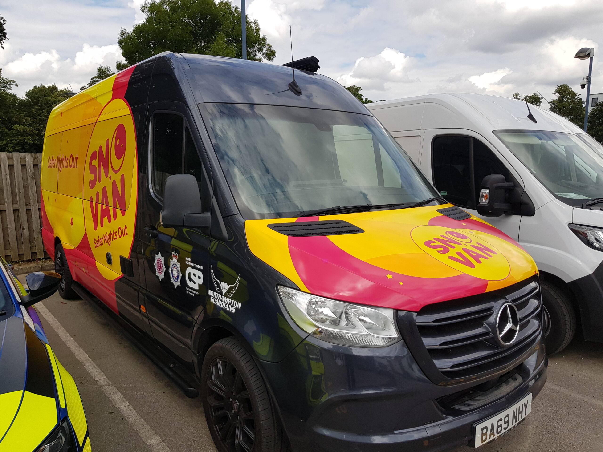 The SNOvan, a black van with a fluorescent logo on the front bonnet, is shown parked between two other vehicles.