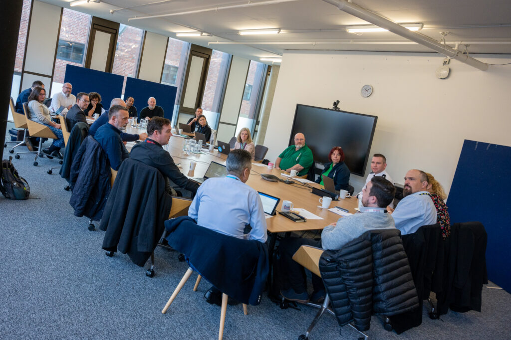 16 people sat around a round table in a meeting room