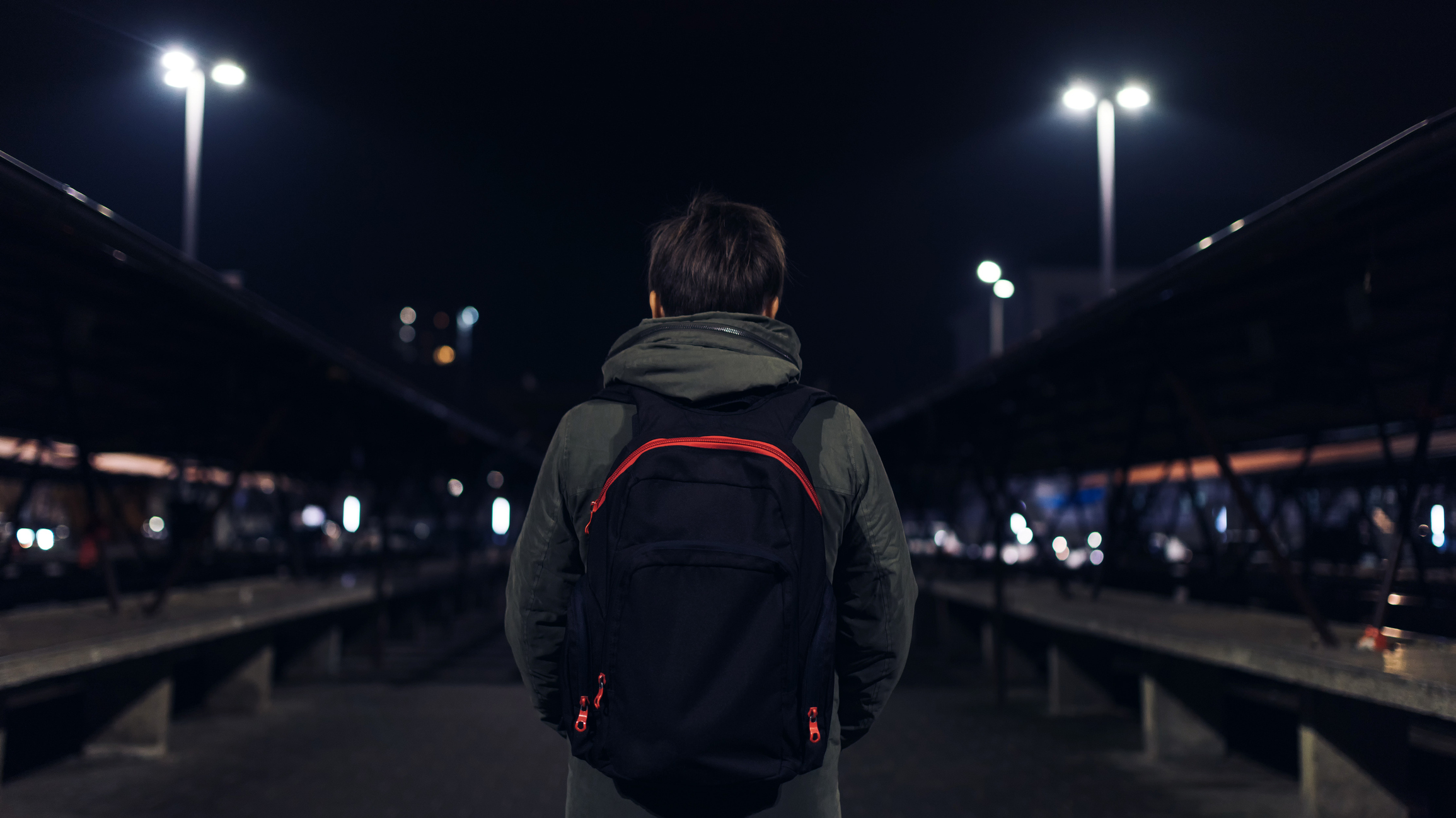 Young Person with their back to the camera wearing a rucksack. Picture at night with street lighting visible