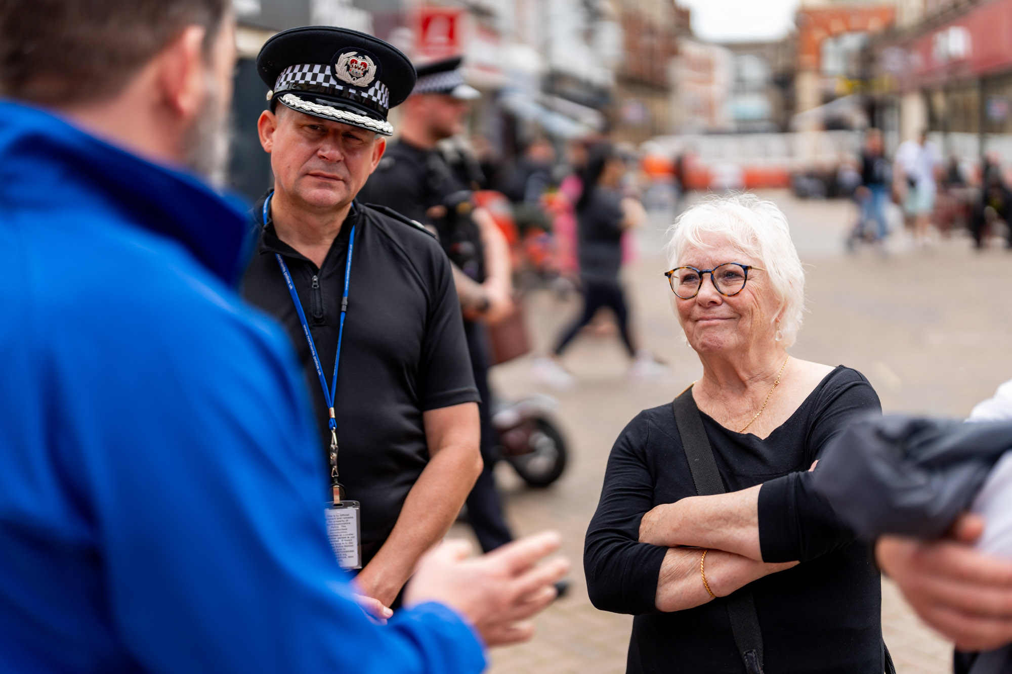 Police, Fire and Crime Commissioner Danielle Stone is pictured on the right wearing a black dress. Next to her, wearing a black police unfiform and hat, is Chief Constable Ivan Balhatchet. On the left, blurred in the foreground, is a man wearing a blue jacket facing them.