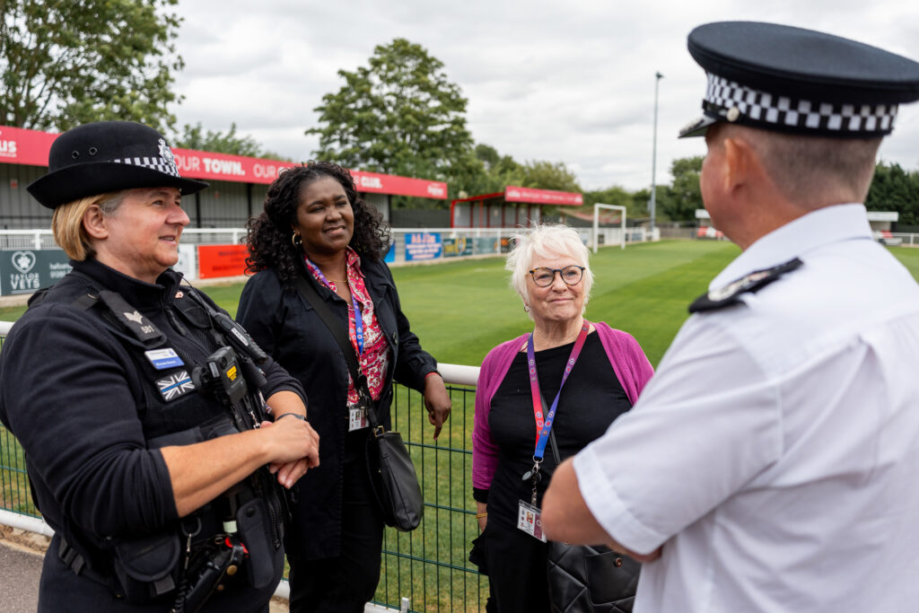 DPFCC Marianne Kimani, PFCC Danielle Stone and Chief Constable Ivan Balhatchet talking to a police officer at Brackley Football Club