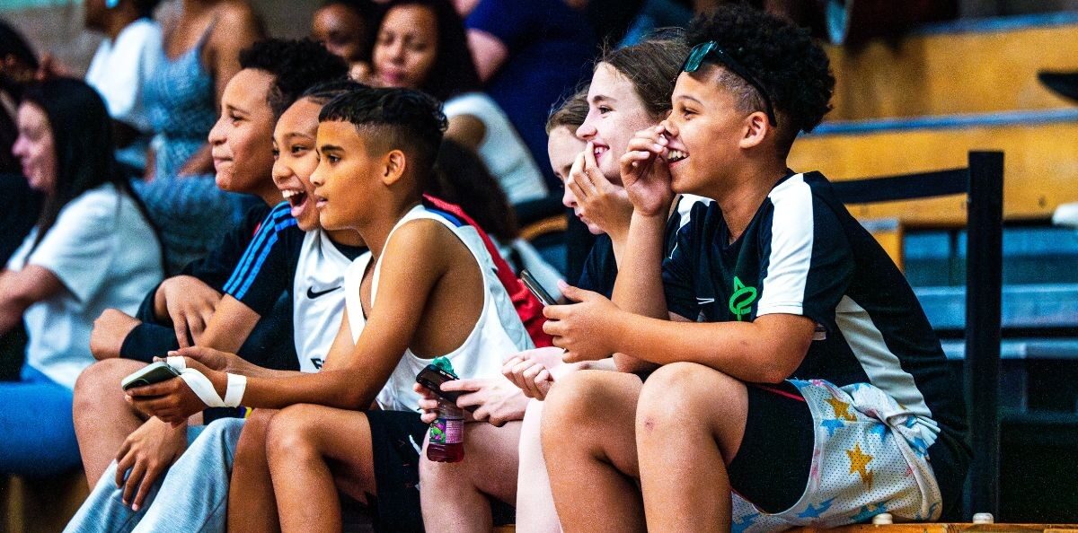 Five children in basketball kit watching a game from the sidelines