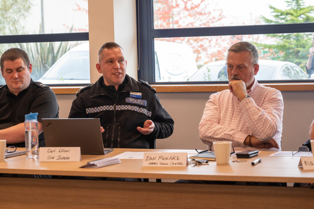 Chief Inspector Carl Wilson, wearing Police uniform talking. Sat next to Dan Pickard from Corby Shopping Centre wearing a white shirt.