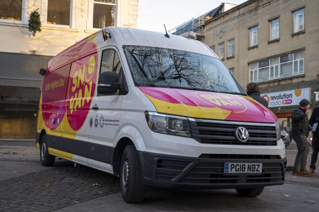 the front of the SNO Van, which is white, with pink and yellow decals with a large SNO VAN logo on the front and side