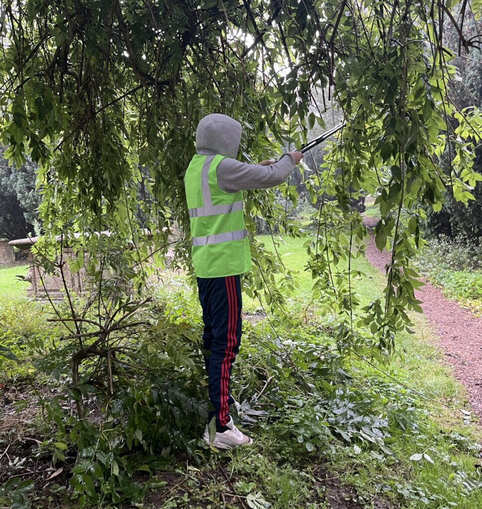 An offender in a hi-vis jacket cuts back a tree at St Lawrence's church