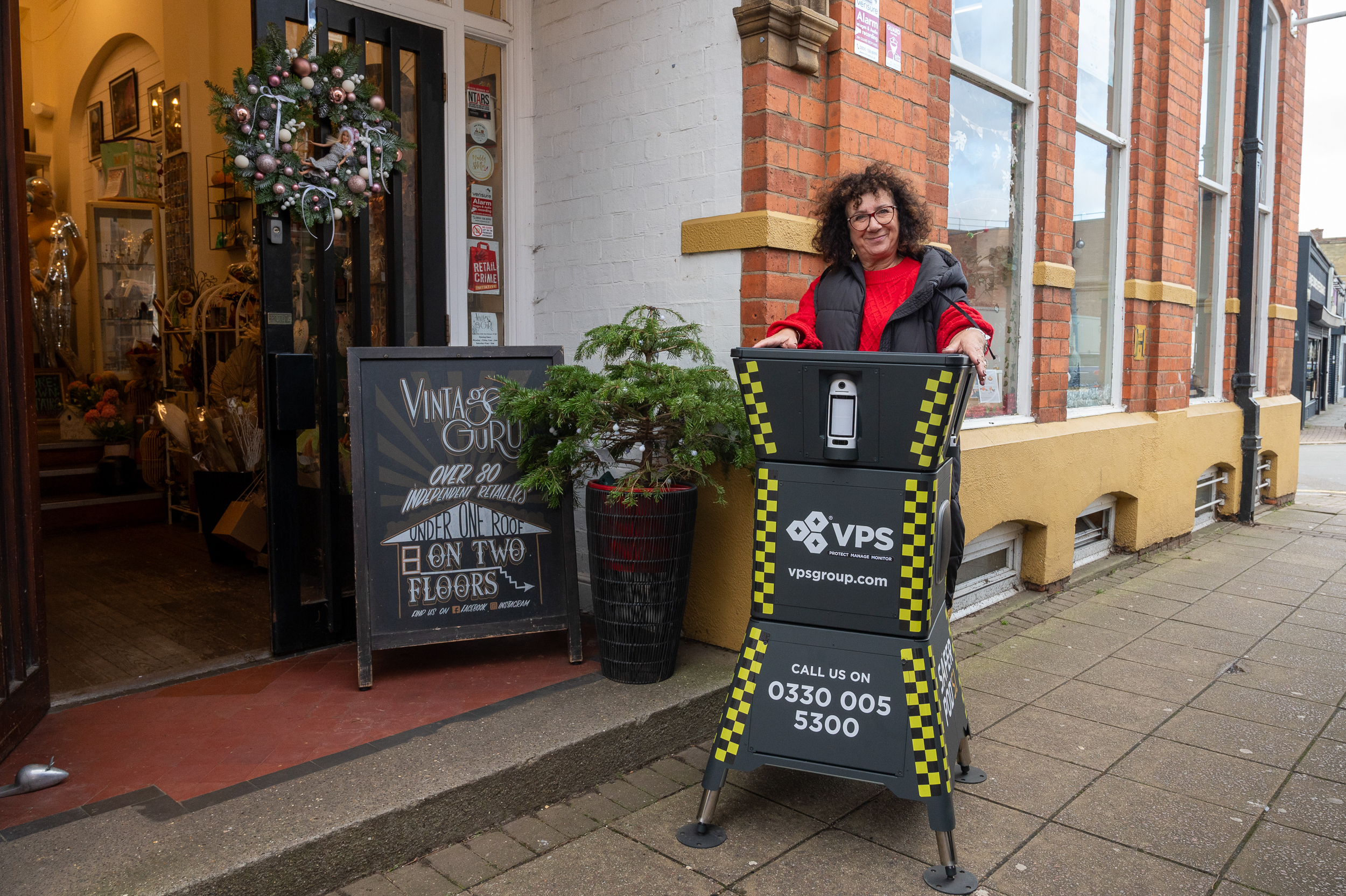 Shop owner Julie Tekman in a red jumper stood in front of her shop sign with a large security robot