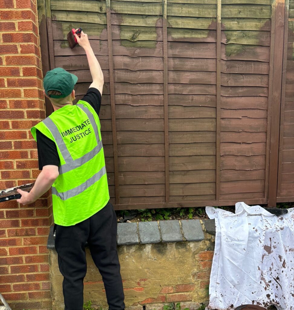 An offender wearing a hi-vis paints a fence