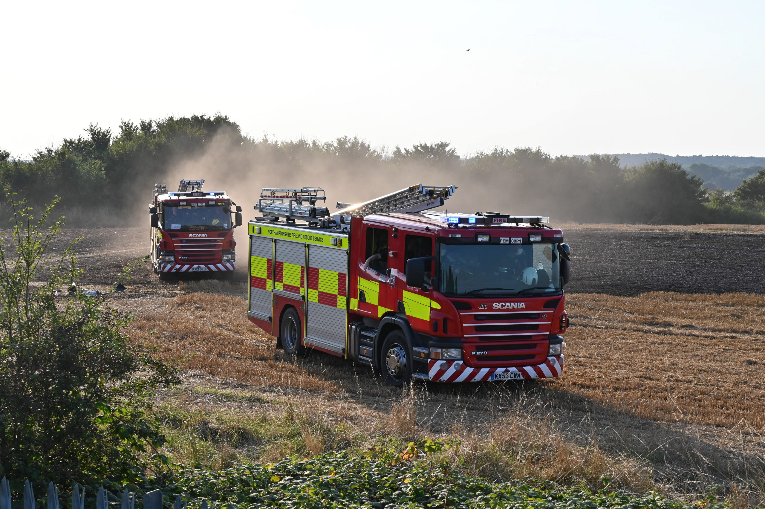 Two fire engines driving through a dry field on their way to a fire