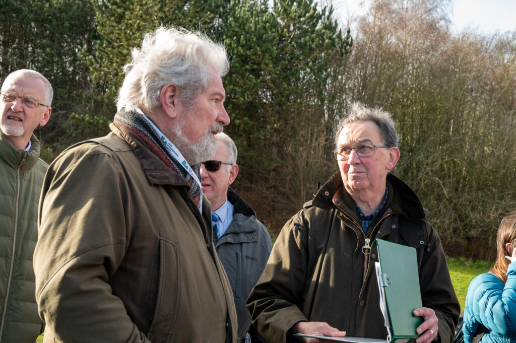 Two men outside talking to each other, both in coats, one of them folding a green folder