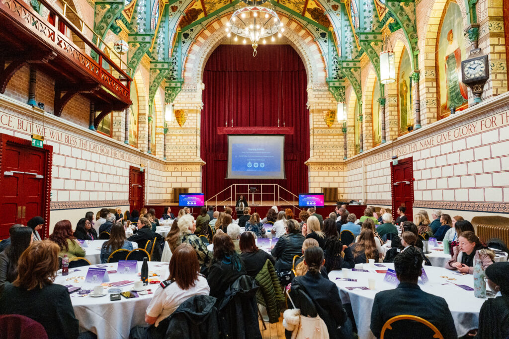 Groups of people sat at round tables in Northampton's guildhall, all looking at a large screen 