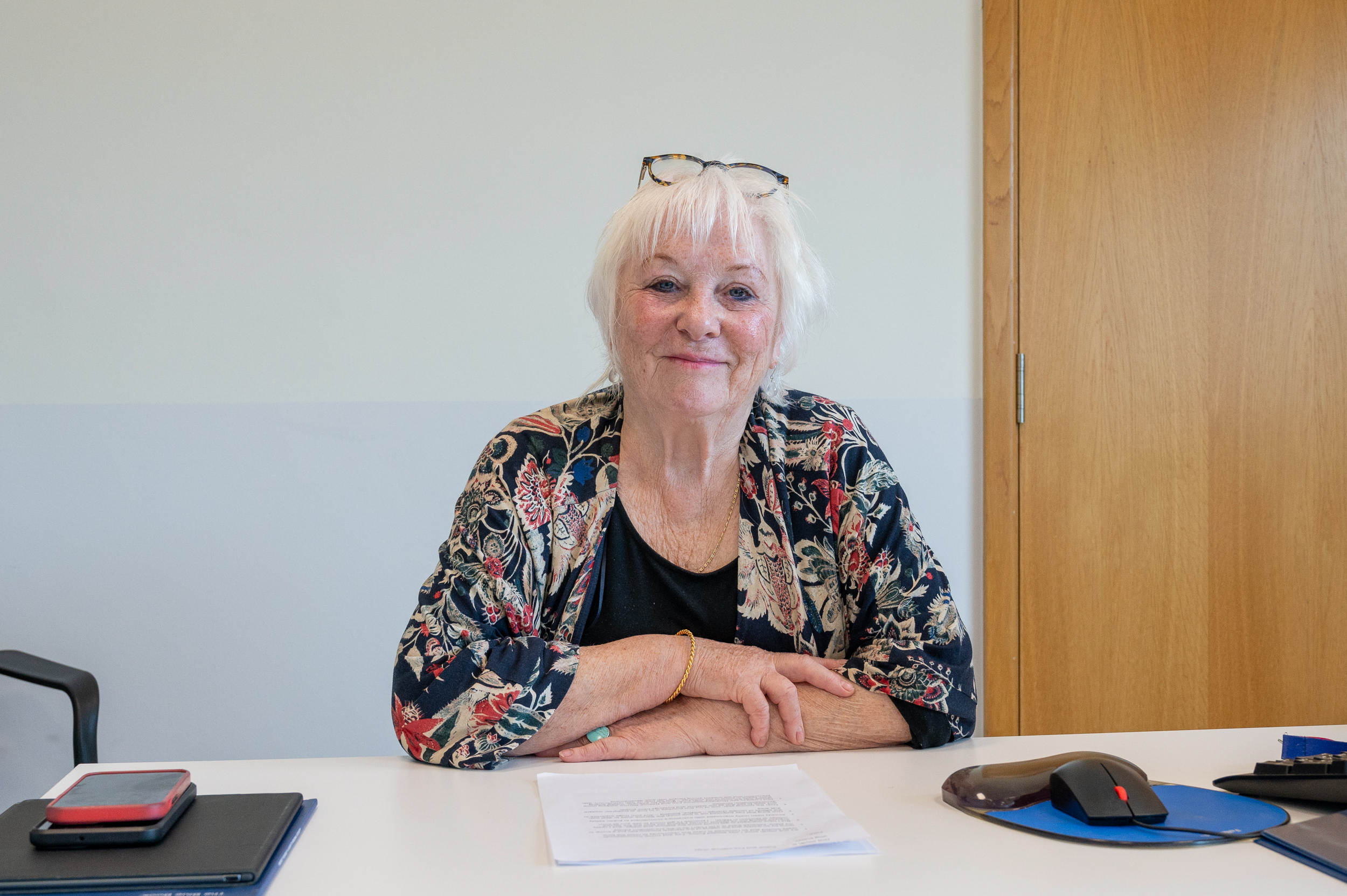 Police, Fire and Crime Commissioner Danielle Stone is wearing a black top and flowery jacket. She is sitting at a white desk,