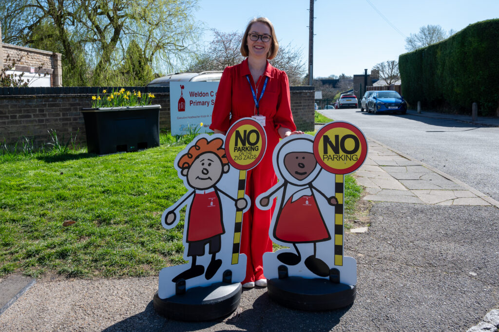 Jane Clowery stands outside Weldon Primary School wearing a red dress and she stands behind the parking buddies.