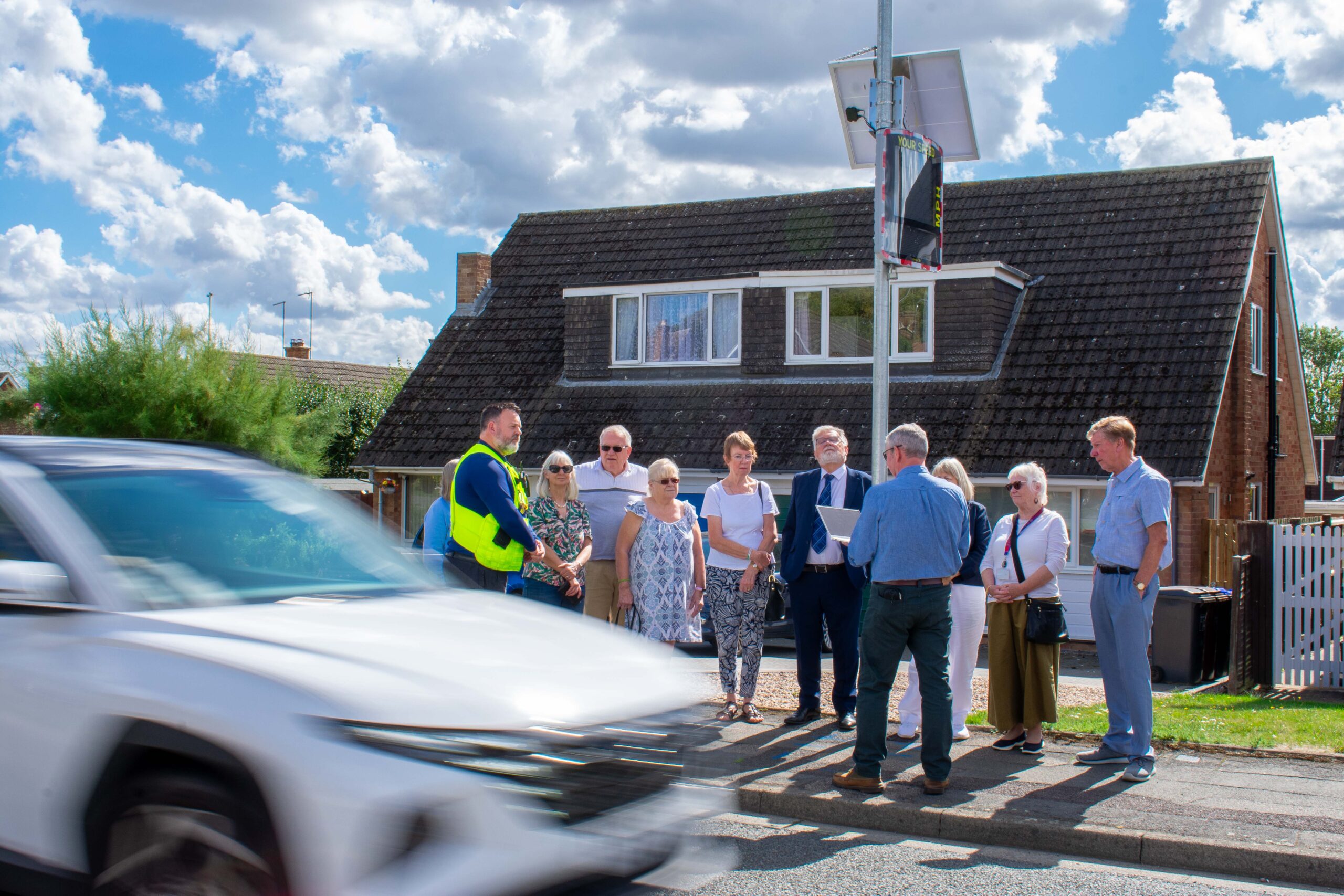 Abington Vale residents stand by the vehicle activated sign as a white car drives by.