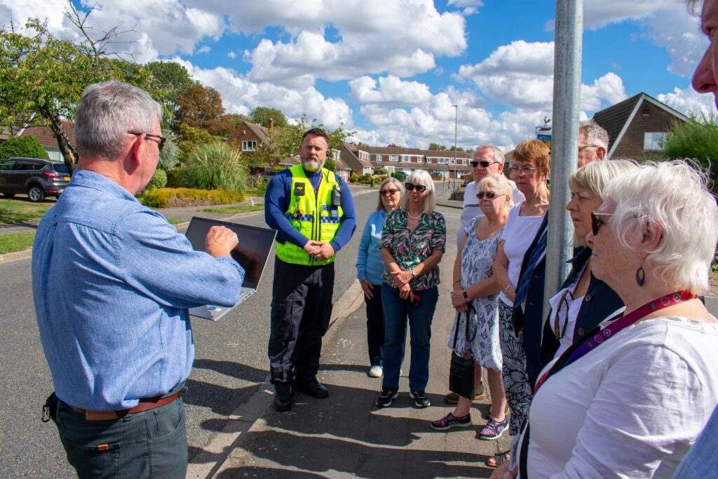Residents talk round a man holding a laptop who holds the data for the speed limit sign.