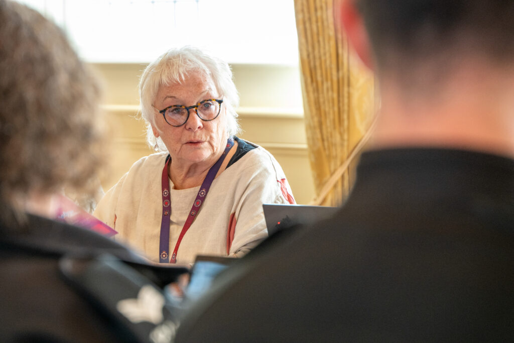 A person in a white top and wearing a police lanyard is shown facing the camera, in between two people who are blurred.