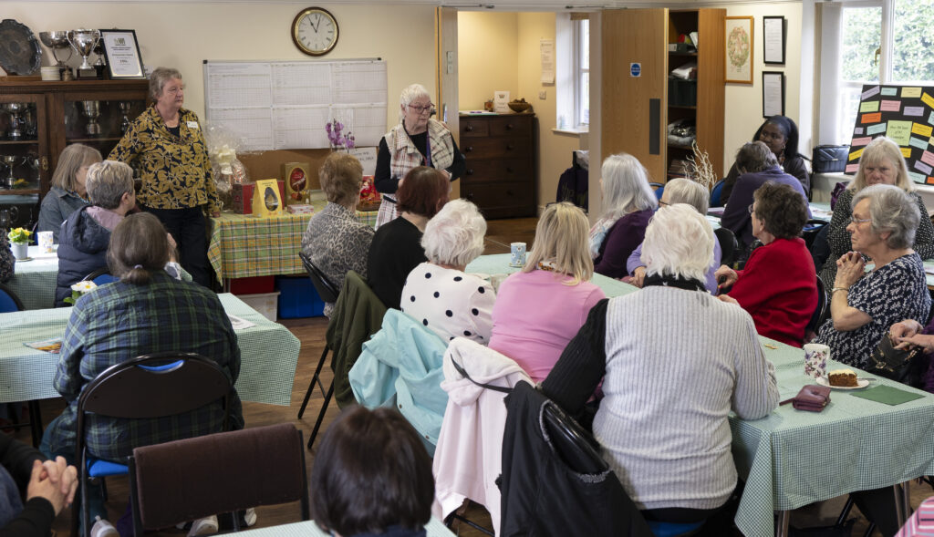 2 women standing in front of a group of women sat at tables